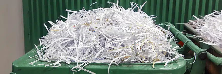 Close-up of a green industrial bin completely overflowing with long strips of shredded paper, illustrating the volume of secured document destruction.