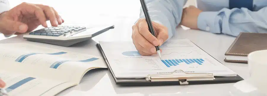 Two people performing an analysis of financial documents together on a white desk surface