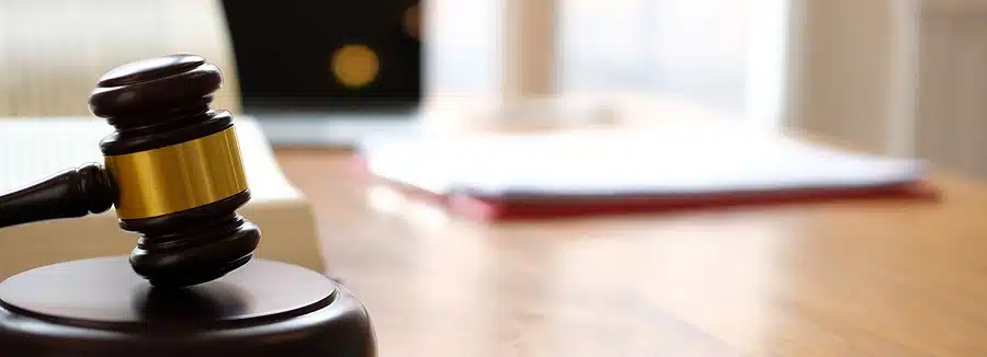 A gavel is sitting on a desk in the foreground while documents are blurred in the background.